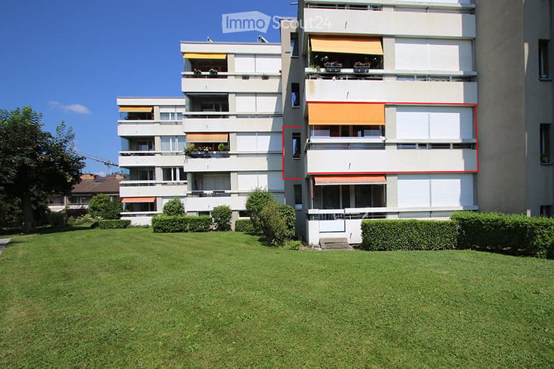 Multi-story apartment building with balconies and a well-maintained lawn in front.