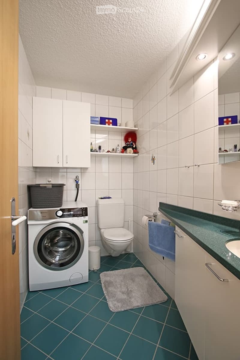 Bathroom with white tiles, a washing machine, toilet, sink, and a small rug on the floor.