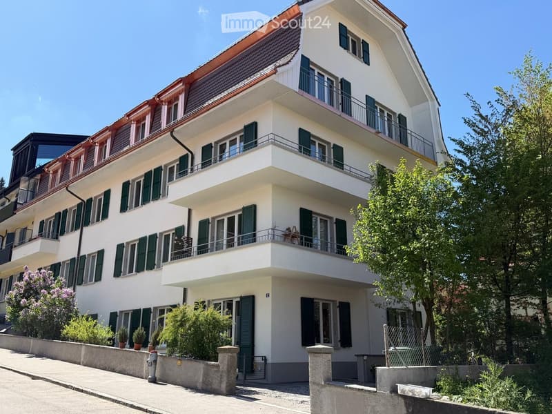 white building, multiple balconies, green shutters, red roof, garden, trees