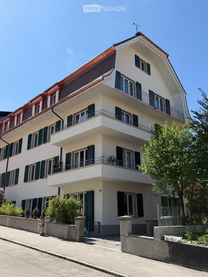 3 story white house, green shutters, balconies, red roof, garden, street view