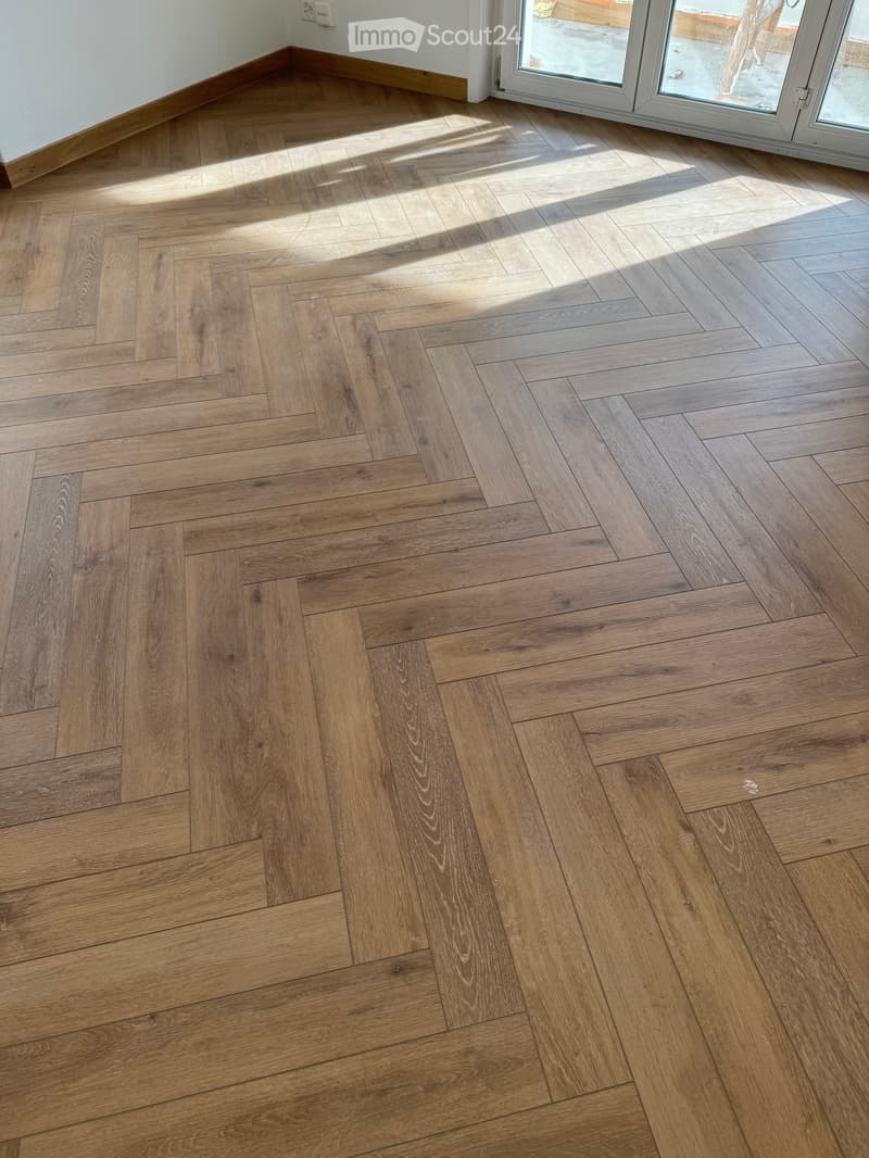 Herringbone wooden floor, sunlit, glass doors to the outside