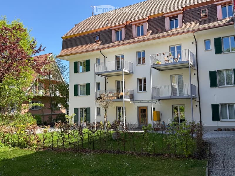 3 story apartment building, white walls, green shutters, balconies, garden, gravel driveway