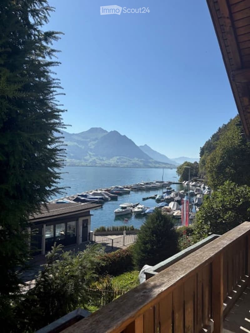 Balcony overlooking a serene lake with docked boats and distant mountains under a clear blue sky.