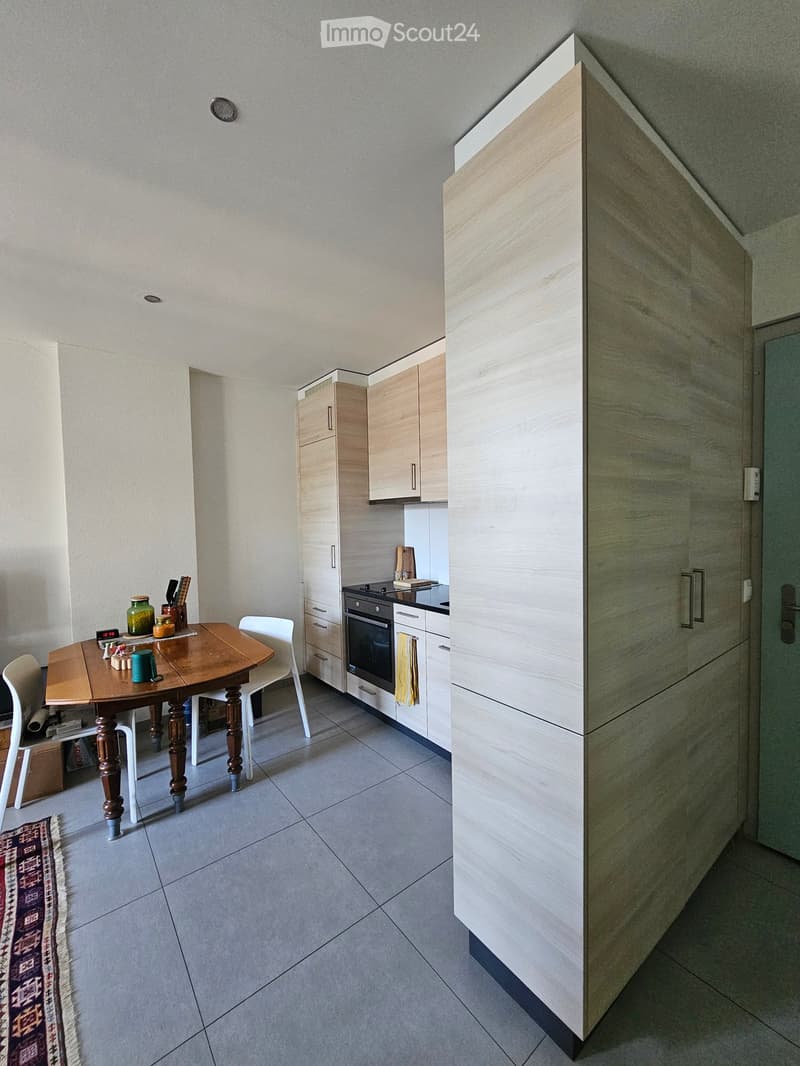Modern kitchen with light wood cabinets, a wooden dining table with chairs, and various kitchen items on the table.