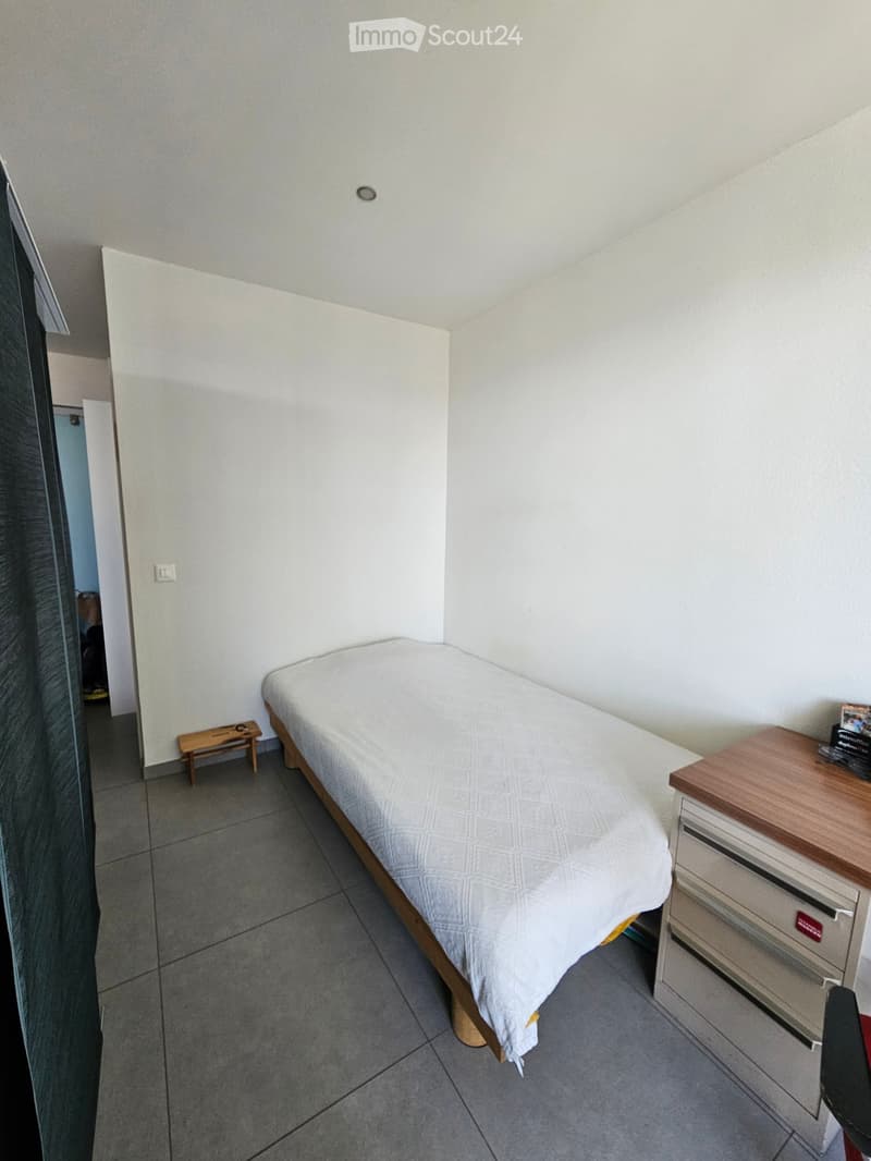 Small bedroom with a single bed, nightstand, and a small wooden stool near the door.