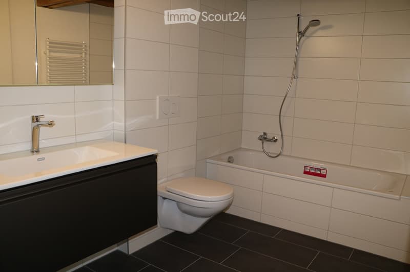 Modern bathroom with white tiles, black floor, sink with faucet, toilet, bathtub with showerhead, mirror, and radiator.