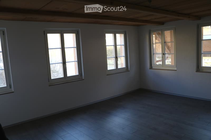 Empty room with wooden flooring and multiple windows, featuring a wooden ceiling and neutral-colored walls.