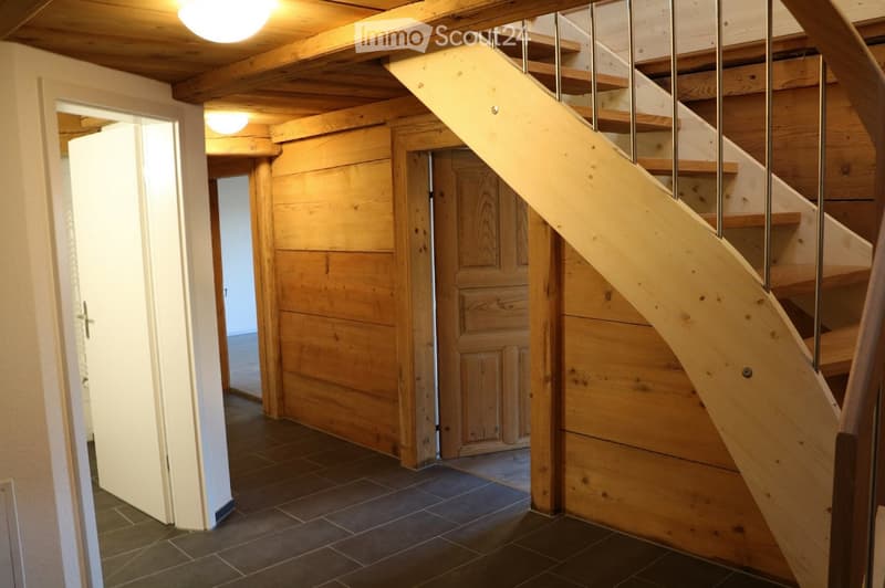 Wooden staircase with metal railing, wooden walls, tiled floor, and open doorway leading to another room.