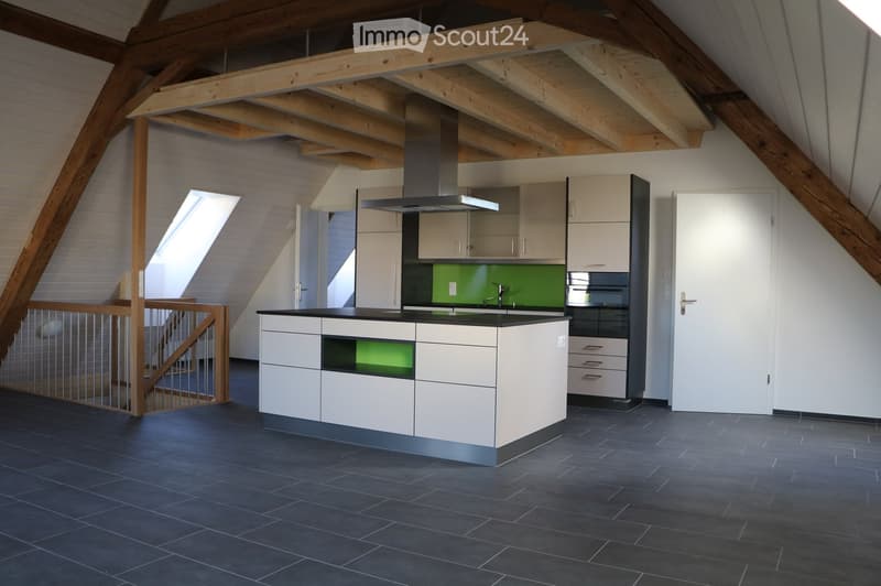 Modern kitchen with white cabinets, black countertops, stainless steel appliances, and a central island. Exposed wooden beams on the ceiling and dark tiled flooring.