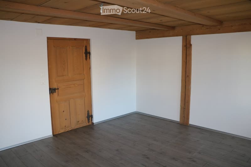 Empty room with wooden floor, white walls, and a wooden door with metal fittings.