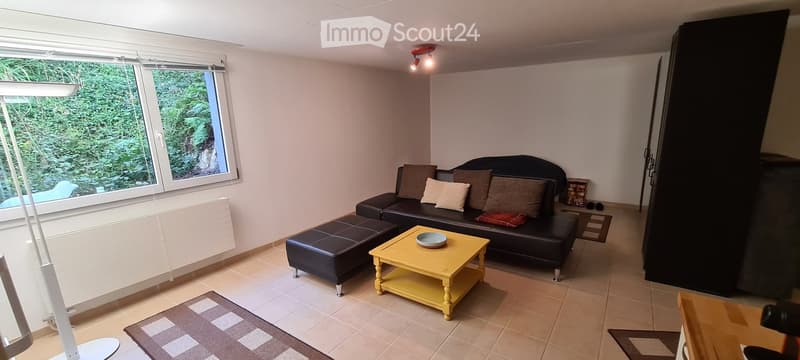 Modern living room with large windows, black leather sofa, yellow coffee table, ottoman, and a patterned rug.