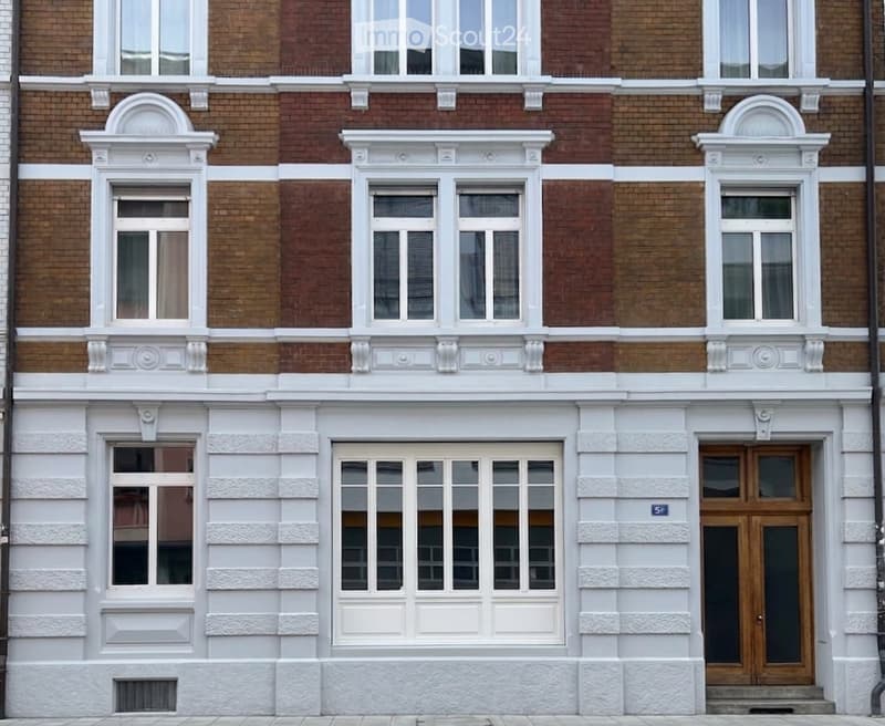Classic European building facade with red brick upper levels and white plaster lower level, featuring multiple windows with decorative white surrounds and a central wooden door.