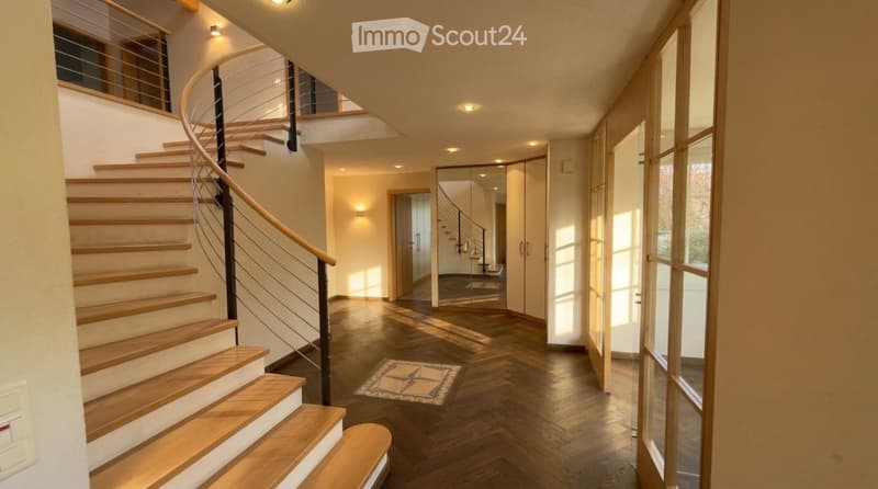 Modern hallway with wooden flooring, a curved staircase with wooden steps and a metal railing, recessed lighting, and large windows allowing natural light to enter.