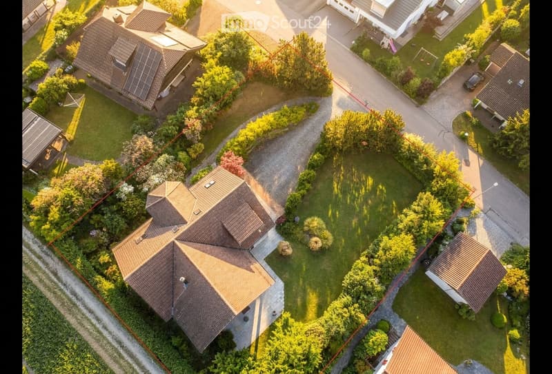 Aerial view of a residential neighborhood with multiple houses, well-maintained gardens, driveways, and solar panels on some roofs.