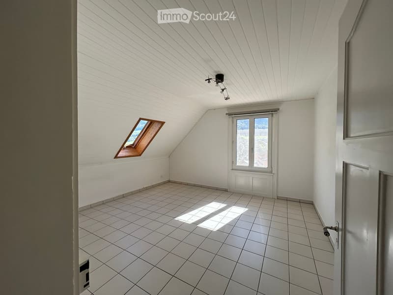 Empty attic room with white walls, tiled floor, skylight window, and large window with blinds.