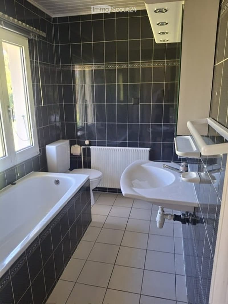 Bathroom with black tiled walls and floor, featuring a bathtub, toilet, sink, and radiator.