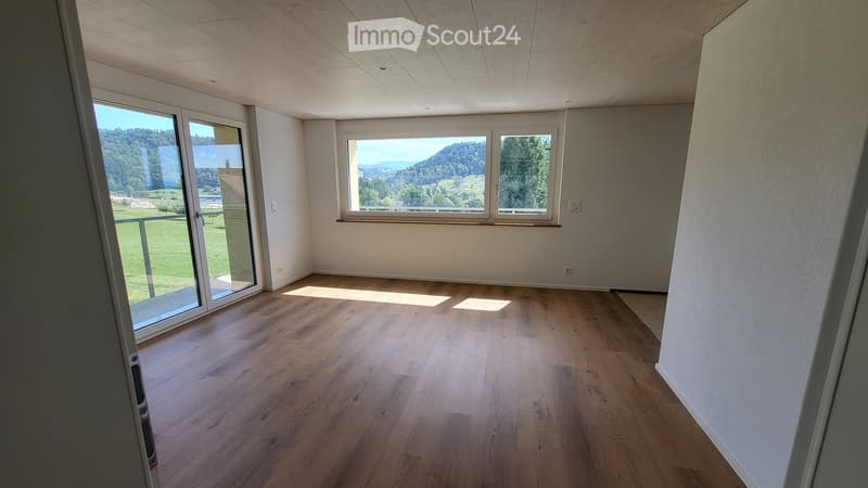 Empty room with wooden flooring, large windows, and a sliding glass door leading to a balcony.