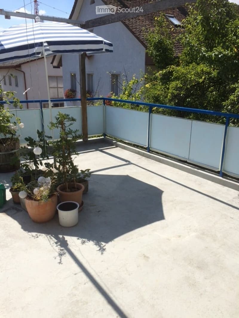 Balcony with potted plants, umbrella, and white railing.