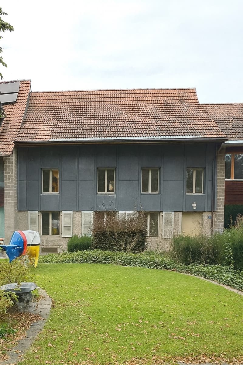 2 story house, gray walls, red tiled roof, several windows, brick foundation, small garden, solar panel on the roof