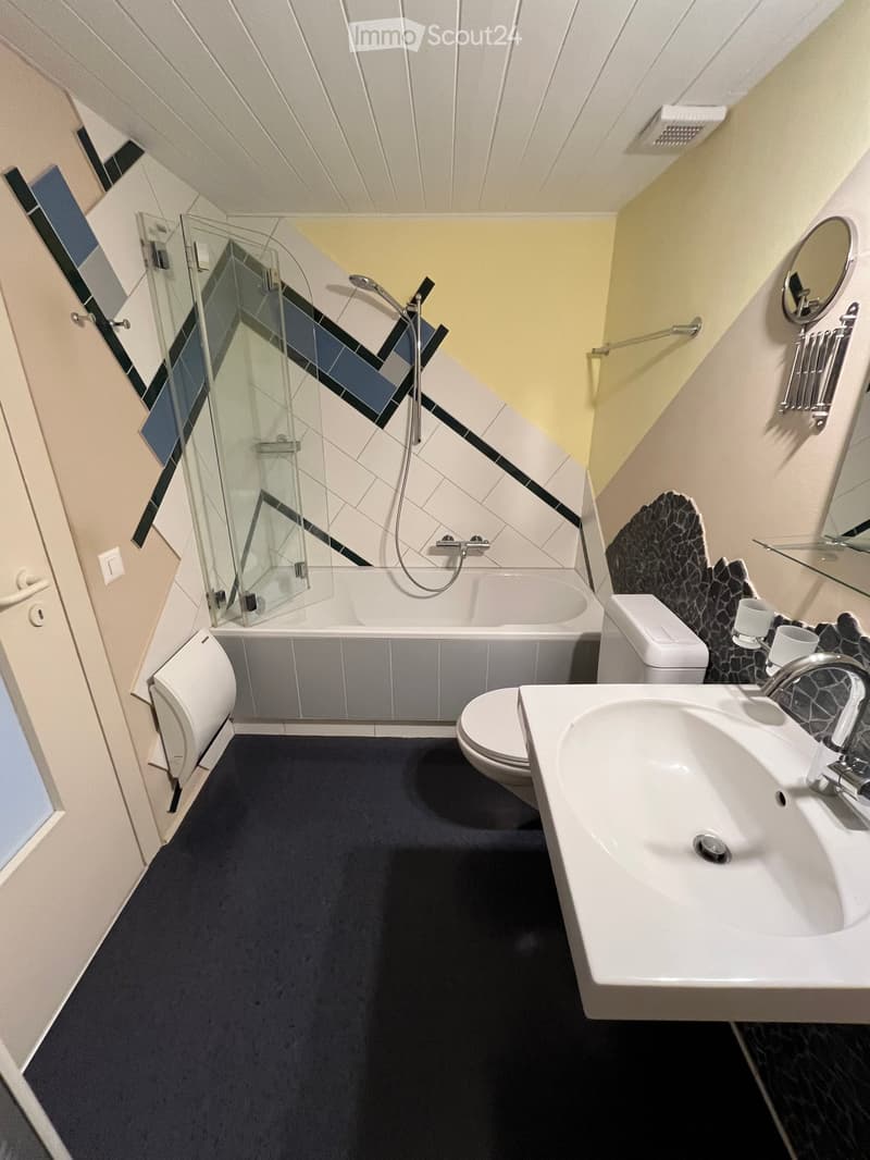 Modern bathroom with a bathtub, toilet, sink, and shower. Features a dark blue carpet, white tiles, and a glass shower enclosure.