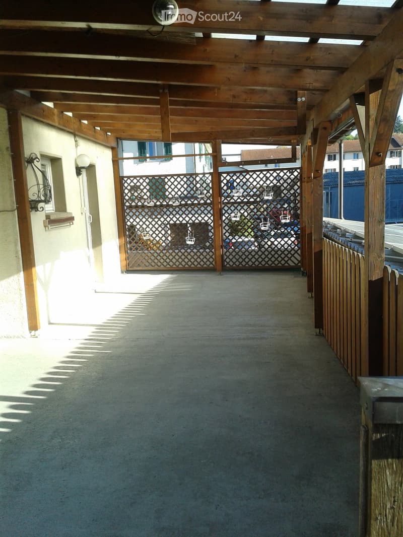 covered terrace with wooden pergola, closed gate, grey paved floor