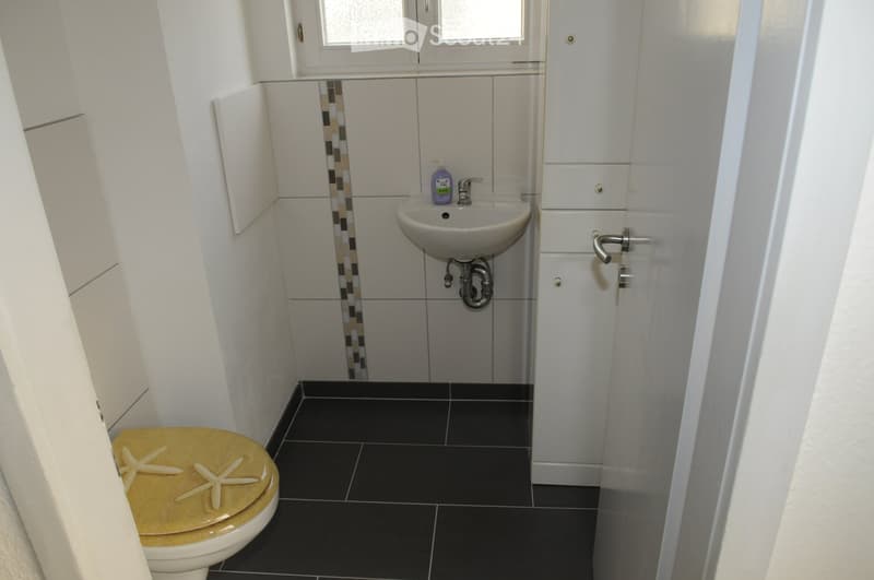 Small bathroom, sink, toilet, white tiled walls, white cabinet, window