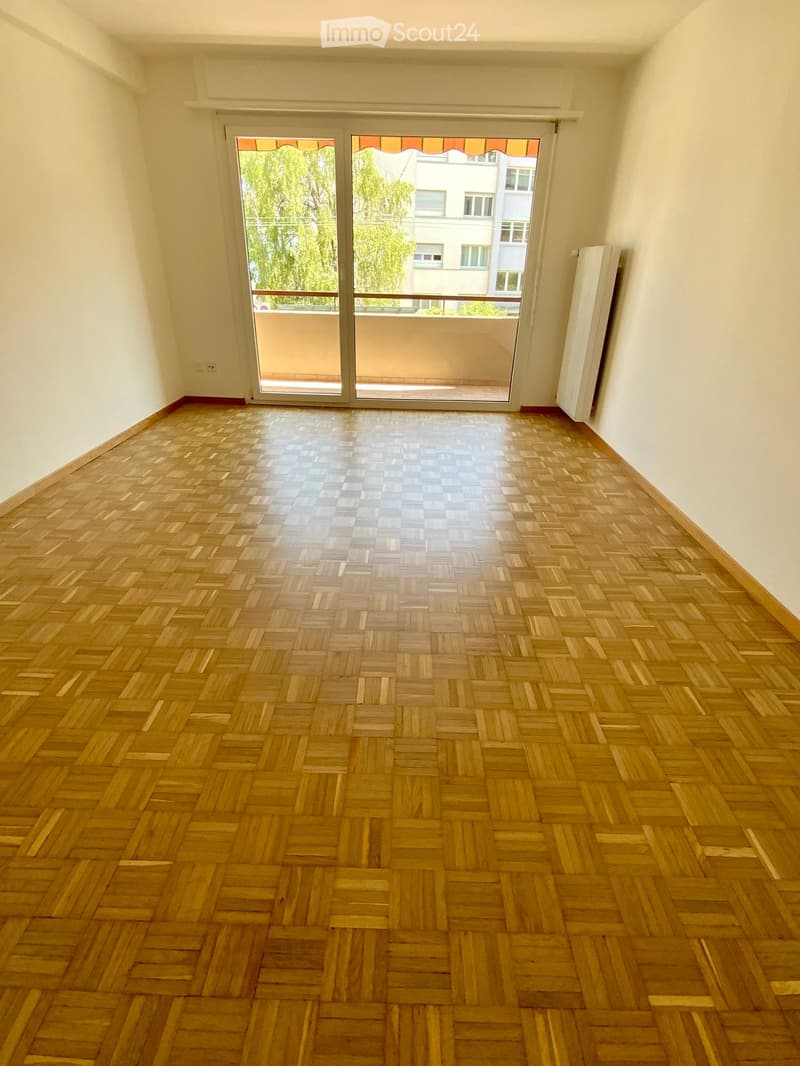 Empty room with wooden parquet flooring, white walls, and a large sliding glass door leading to a balcony.
