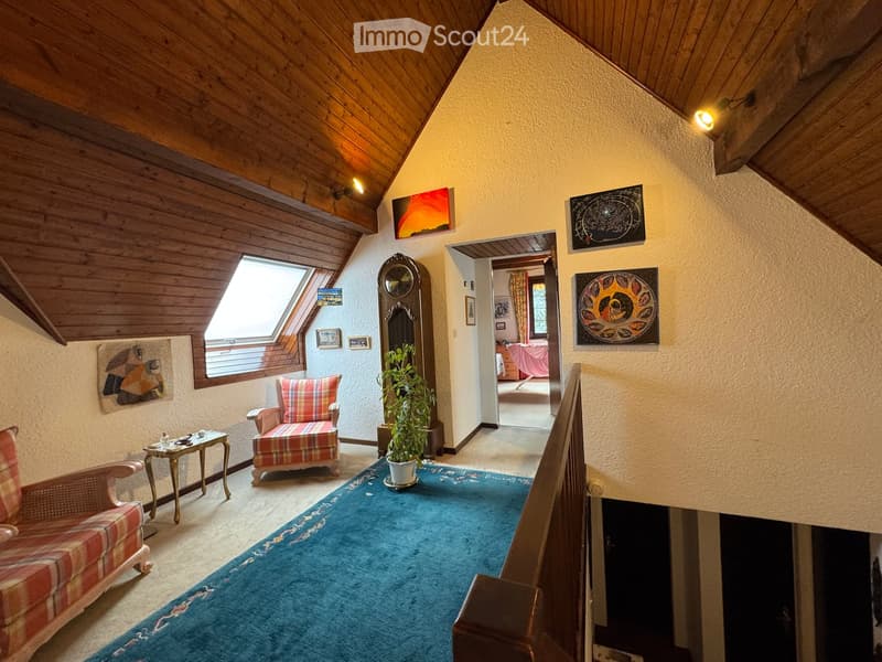 Cozy hallway with wooden ceiling, blue carpet, plaid sofa, small table, plant, and artwork on walls.