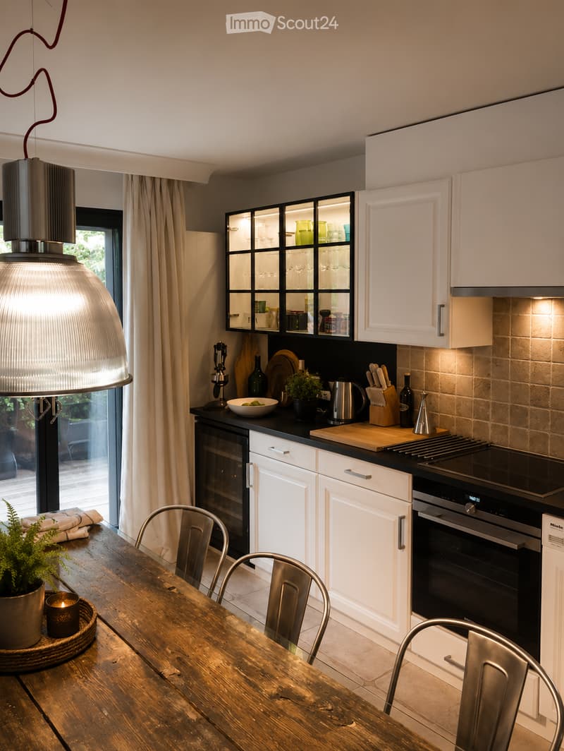 Modern kitchen with white cabinets, black countertops, stainless steel appliances, wooden dining table, and metal chairs.