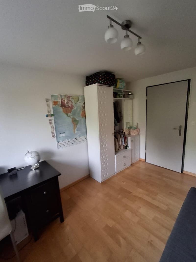 Bedroom with wooden flooring, white wardrobe, nightstand with globe, map on wall, and ceiling lamp.