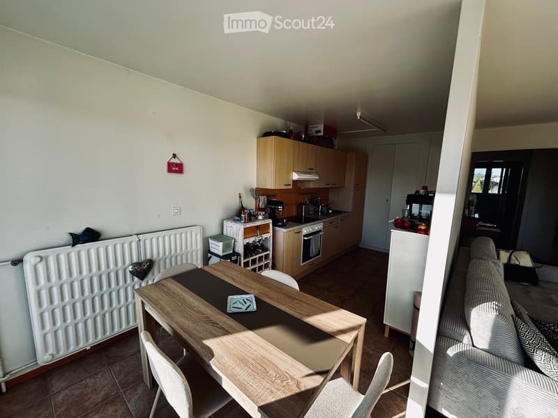 A modern, open-plan living and dining area with a sofa, dining table, and kitchen appliances including an oven and refrigerator.