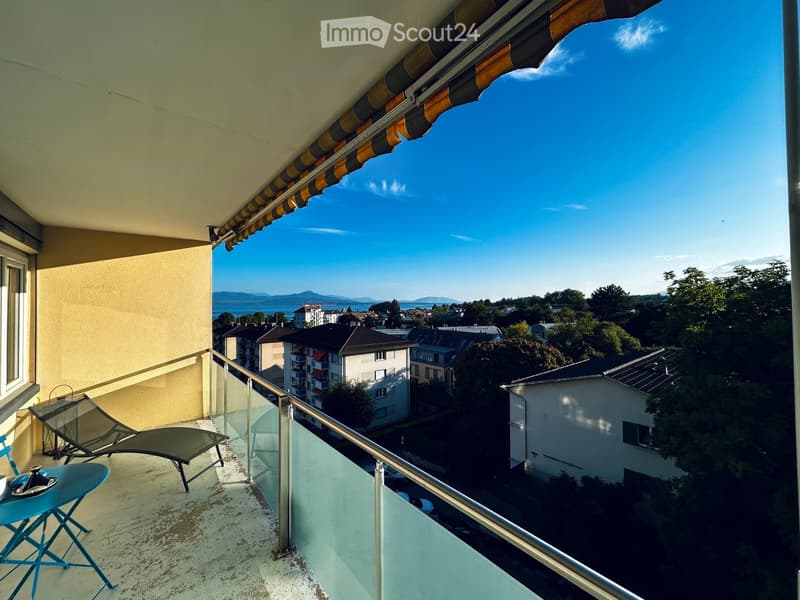 Balcony with a view of the city and lake, featuring a table, chairs, and a lounge chair.