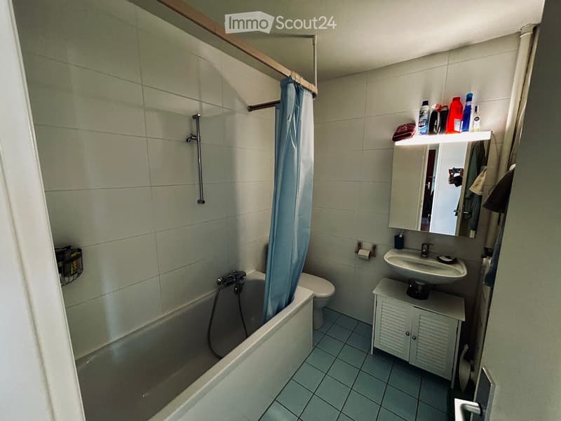 Bathroom with a bathtub, toilet, sink, mirror, and cabinet. Shower curtain is visible, and the walls are tiled.
