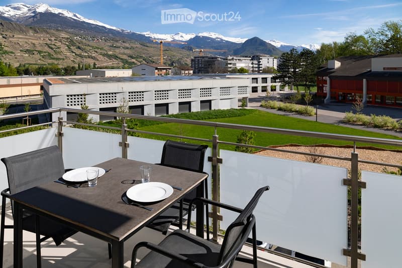 Balcony with a table and chairs, overlooking a green lawn and distant mountains.