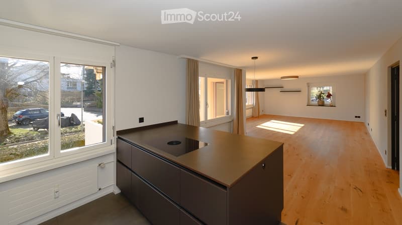 Bright, open-plan room with wooden flooring, large windows, and a modern kitchen island. The space is empty, with no furniture or appliances.