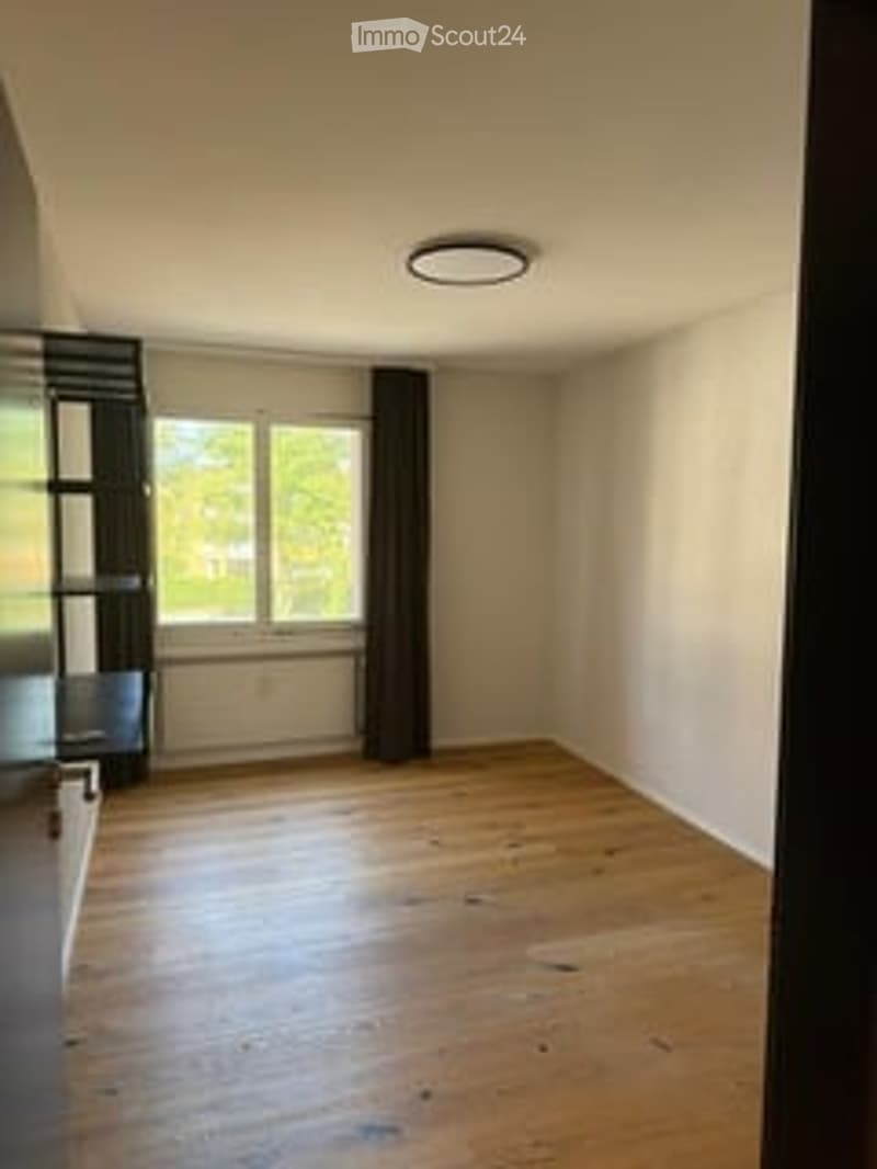 Completely empty room with wooden flooring, white walls, and large windows. No furniture or equipment present.
