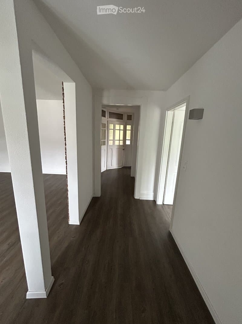 Empty hallway with dark wooden flooring, white walls, and multiple doors leading to other rooms.