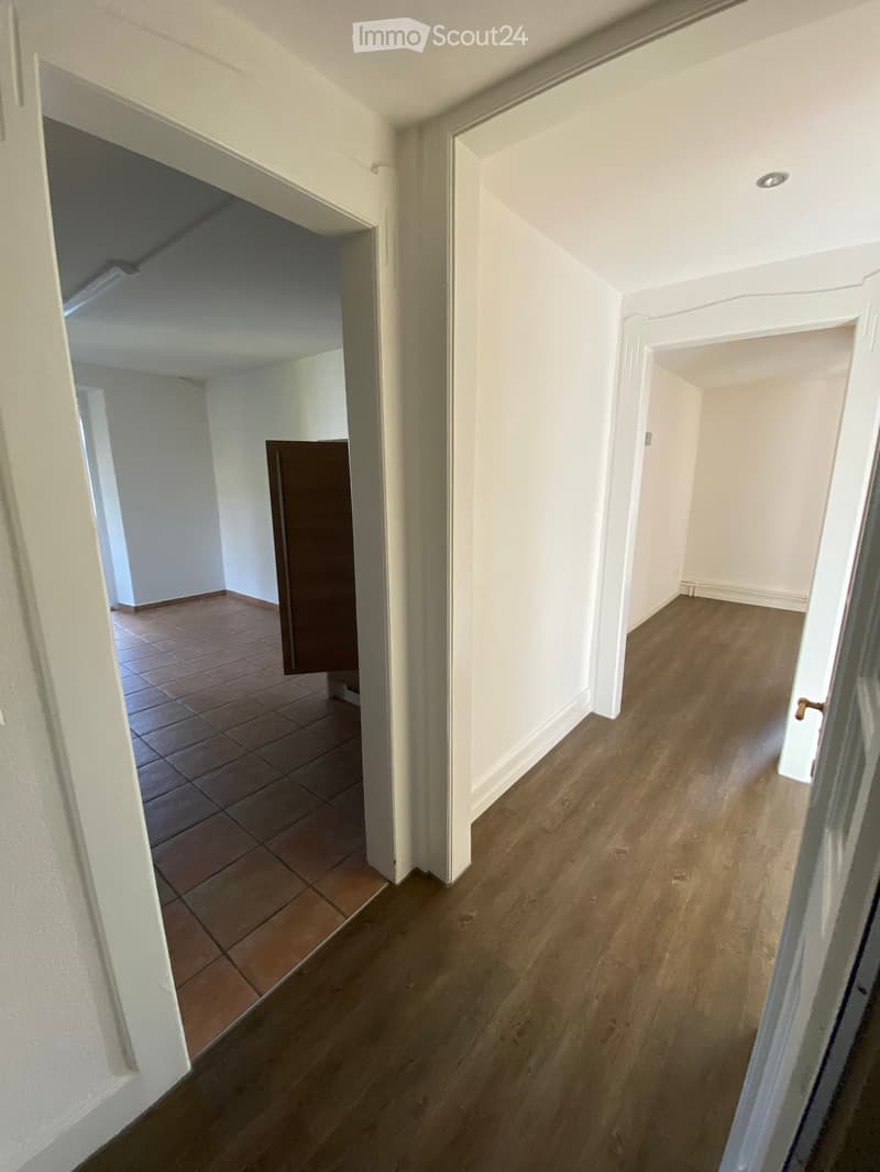 Empty hallway with wooden flooring and white walls, featuring multiple doors leading to other rooms.
