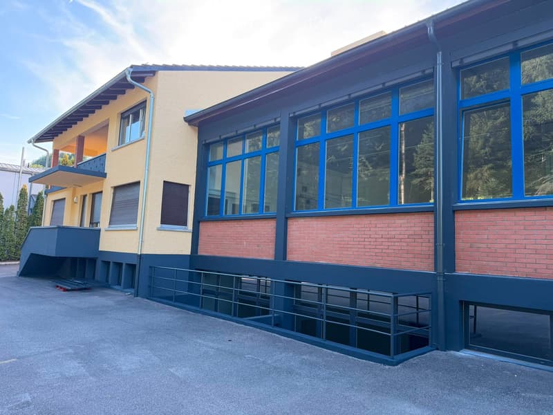 Two-story building with a combination of yellow and red brick facades, large blue-framed windows, and a modern design featuring a raised ground floor and a balcony area.