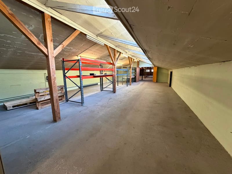 Empty warehouse space with concrete floor, wooden beams, metal shelving units, and a few wooden pallets. No furniture or equipment.