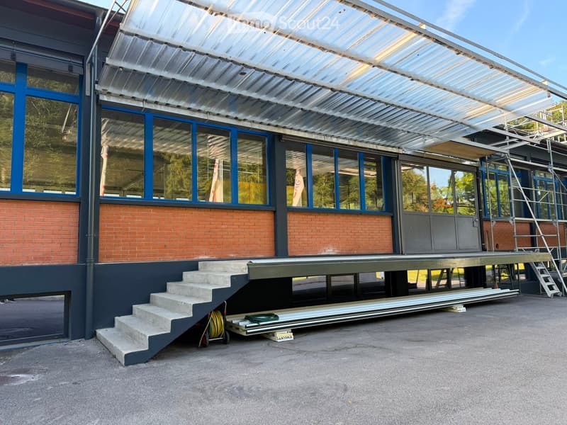 Modern building with a raised ground floor, brick facade, large windows, and a covered walkway leading to a raised platform.