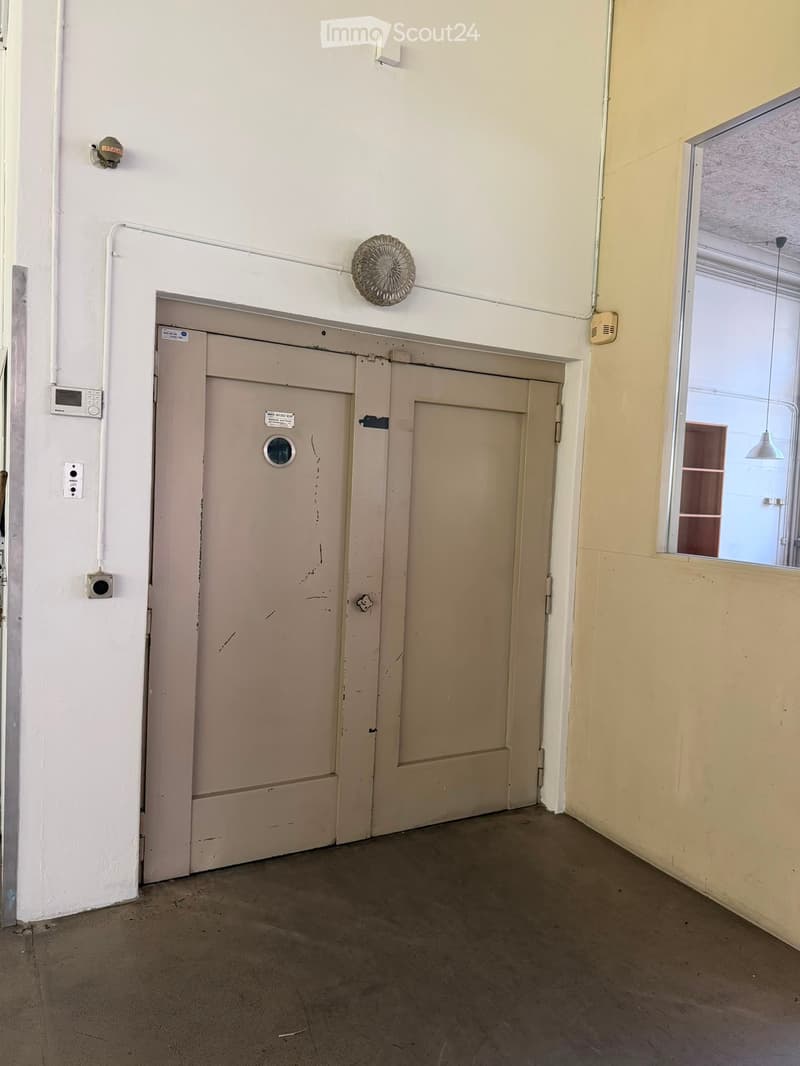 Empty hallway with two closed doors, a small window, and basic wall fixtures.