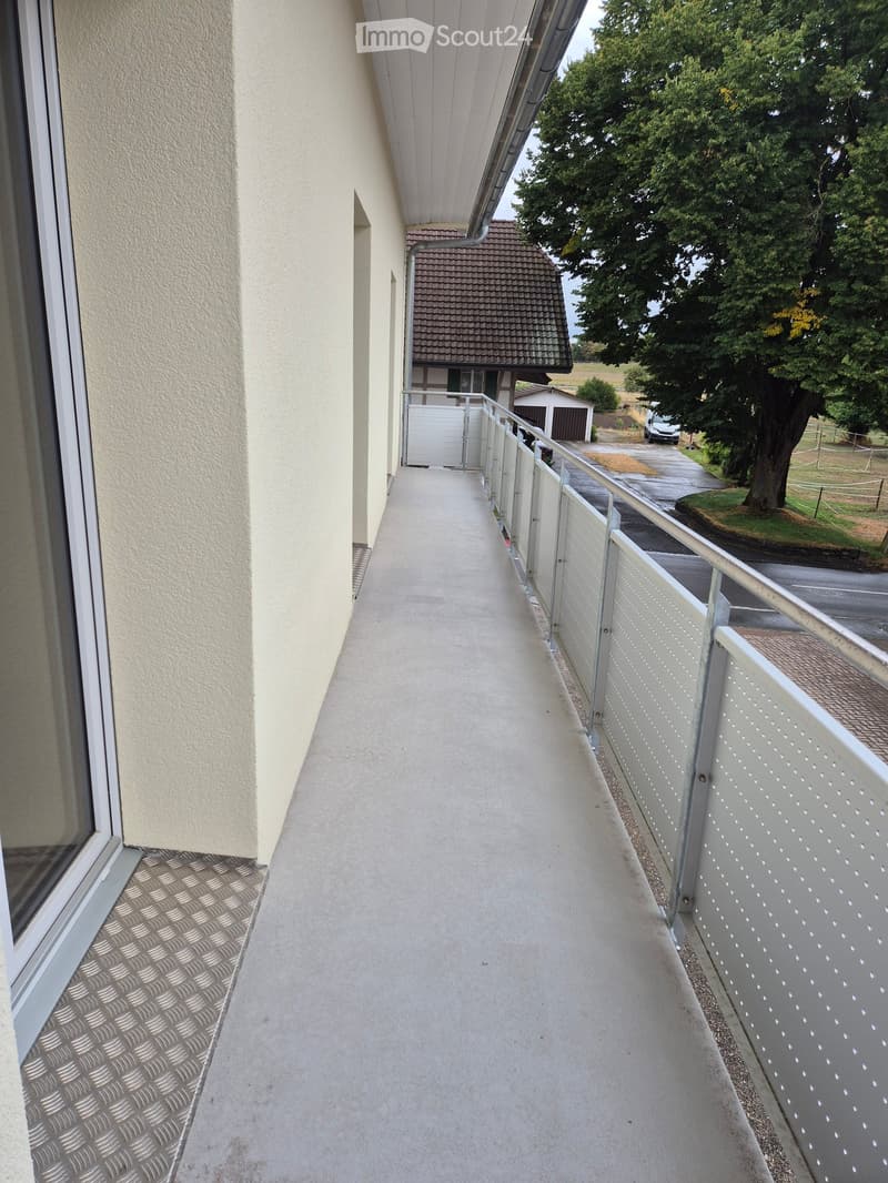 Balcony with metal railing, concrete floor, and a view of a house and driveway.