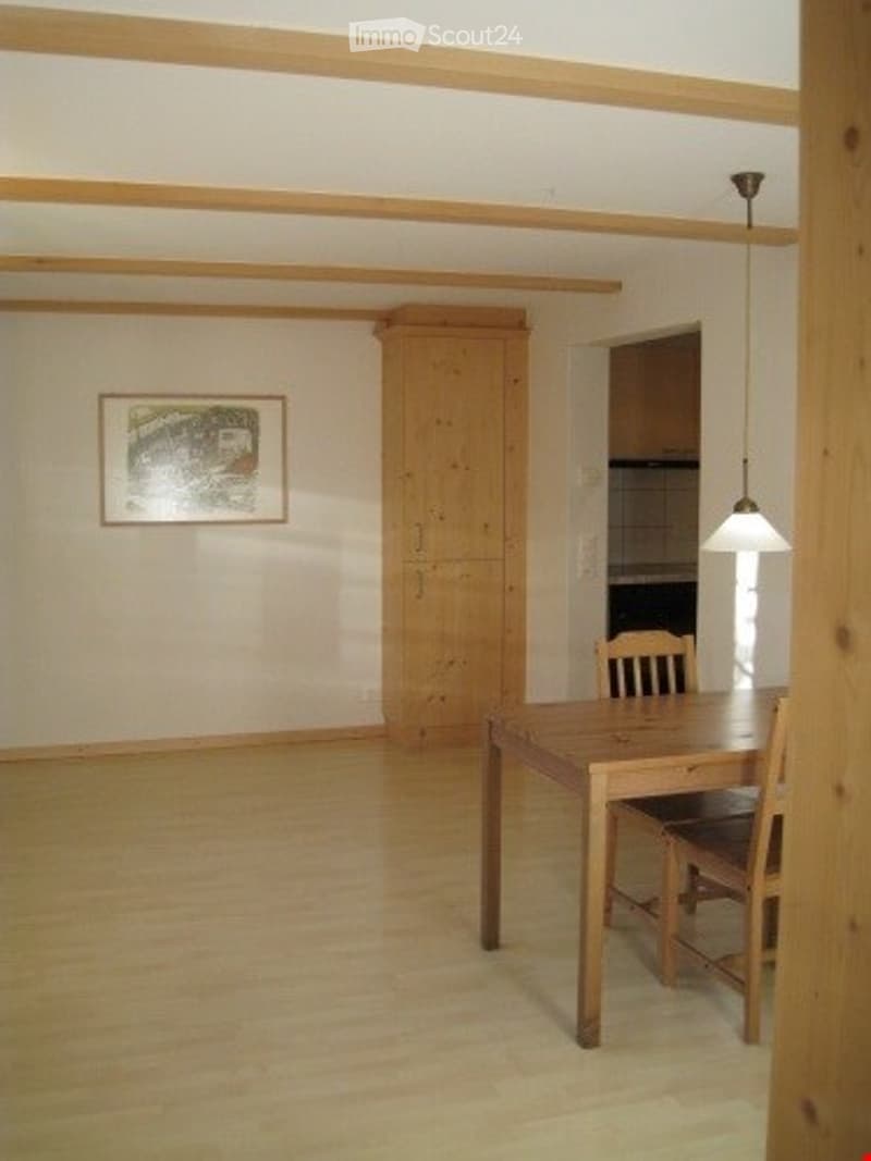 Bright dining area with wooden floor, a dining table with chairs, a tall wooden wardrobe, and a framed picture on the wall.