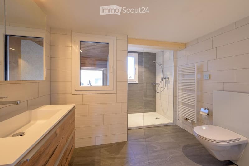 Modern bathroom with a white sink, toilet, glass-enclosed shower, and a white radiator. The walls are tiled in light beige, and the floor is wooden.