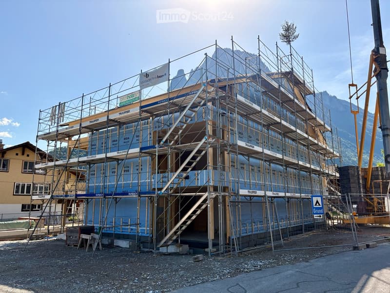 A multi-story building under construction, covered in scaffolding and protective sheeting, with visible construction materials and signage.