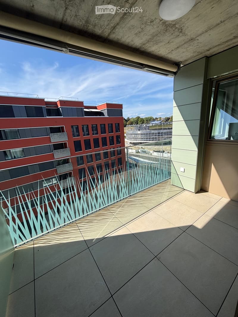 Balcony with tiled floor, modern railing, and view of a red building and surrounding area.