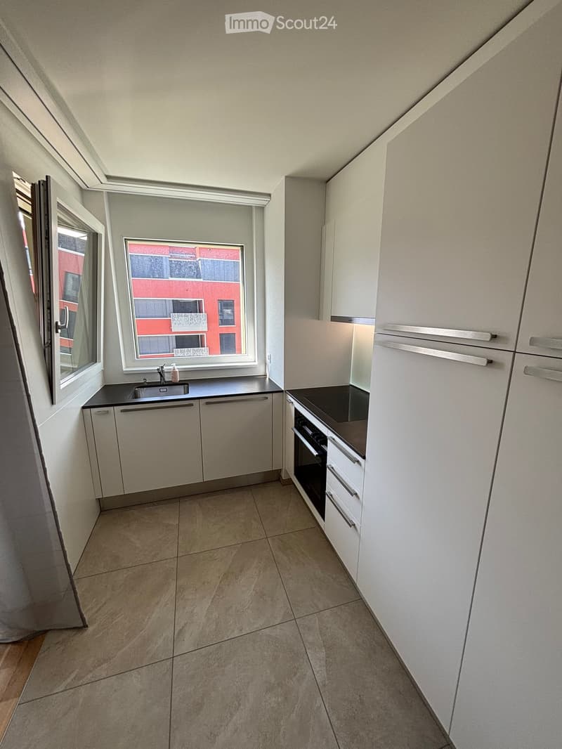 Modern kitchen with white cabinets, a sink, and an oven. The space features tiled flooring and large windows offering a view of the exterior.