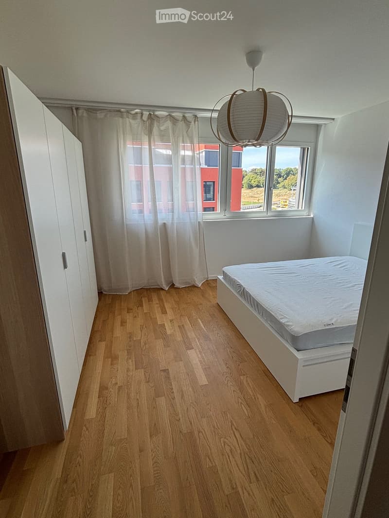 Minimalist bedroom with a single bed, white wardrobe, large window with sheer curtains, and a modern pendant light fixture.