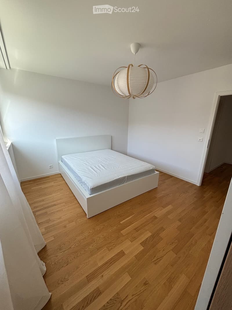Minimalist bedroom with a white bed frame, wooden flooring, and a modern pendant light fixture.